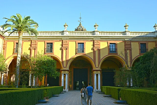 The baroque facade of the Gothic Palace over the Patio del Crucero, with a palm tree and clipped hedges