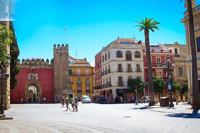 The Puerta del León and its crenellated tower on Plaza del Triunfo, under a blue sky