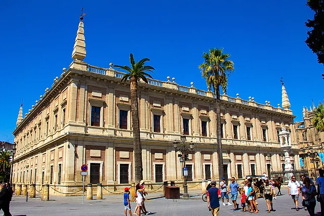The Archivo General de Indias, the former Casa Lonja, with palm trees and a blue sky